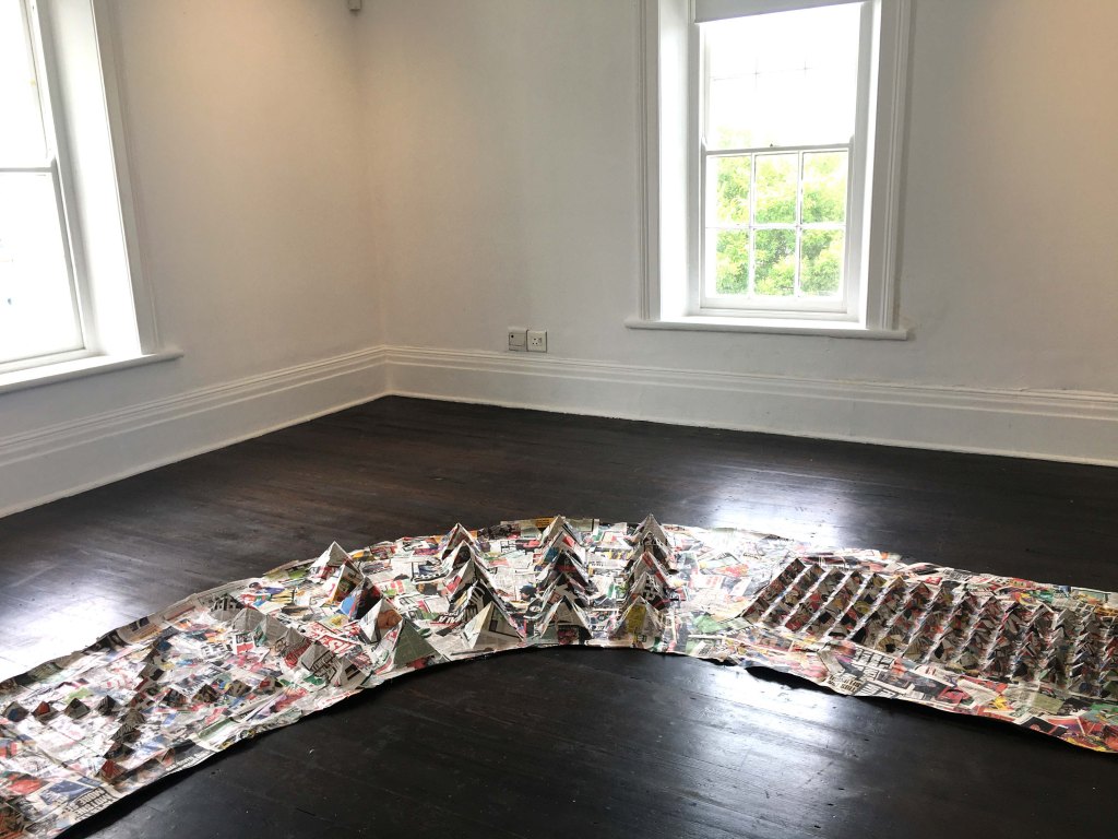 Newspaper installation titled "Amabheqe emihla ngemihla" (2023), featuring variable arrangements of printed material referencing isiZulu petroglyphs and their relevance in everyday life.