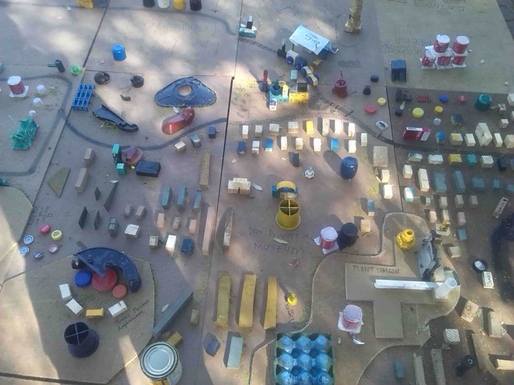 Public installation composed of colourful found objects arranged on a softwood contour map, created during a civic engagement intervention at Vrystaat Kunstefees 2016 in Bloemfontein.