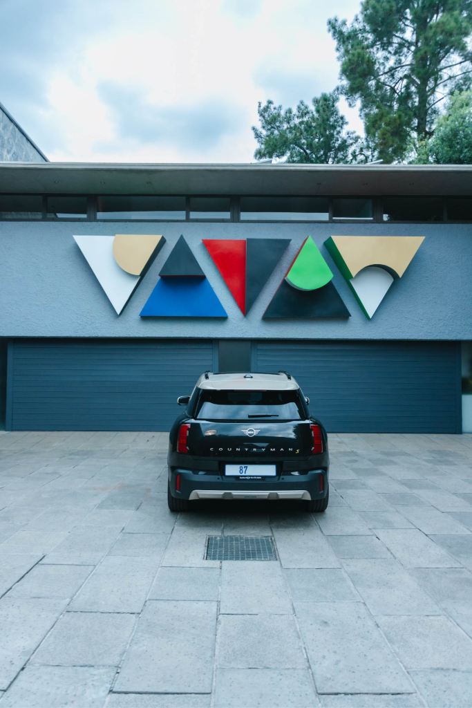 Colourful geometric triangular steel reliefs mounted in a horizontal row on the exterior wall above a garage door.