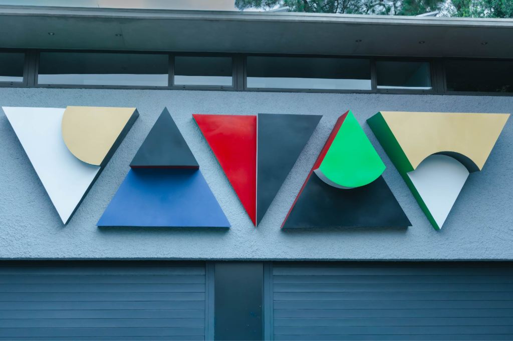 Colourful geometric triangular steel reliefs mounted in a horizontal row on the exterior wall above a garage door.